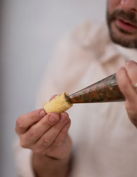Šéfkuchař plní malé křupavé rolky pomocí cukrářského sáčku 