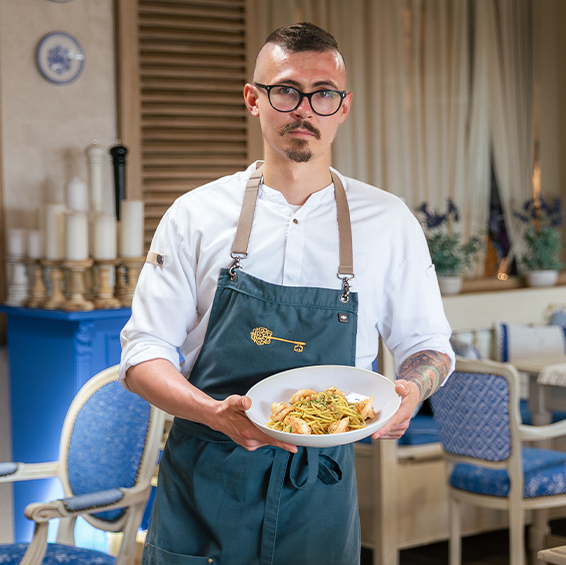 Šéfkuchař drží talíř se špagetami a krevetami v interiéru restaurace 